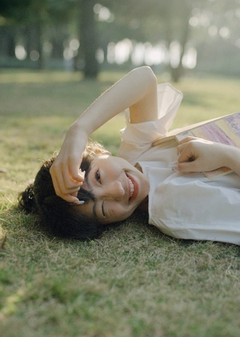 一位穿着白色连衣裙的年轻女子躺在公园的草地上 她的头上有一个女人的脸。