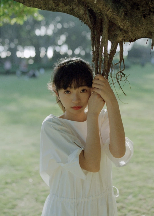 一位穿着白色连衣裙的年轻女子 正把头藏在树底下。