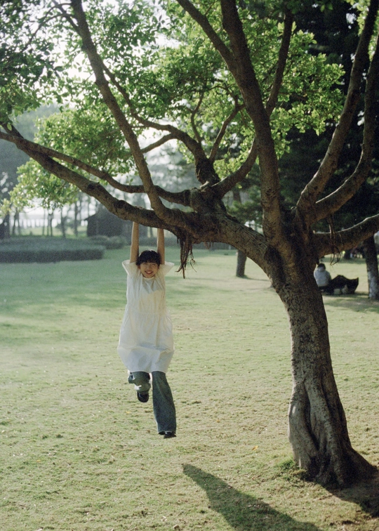 一个小女孩穿着白色衣服从公园的一棵树上跳下来