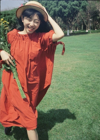 一位穿着橙色连衣裙和帽子 手拿红花的年轻女子在田野中行走。