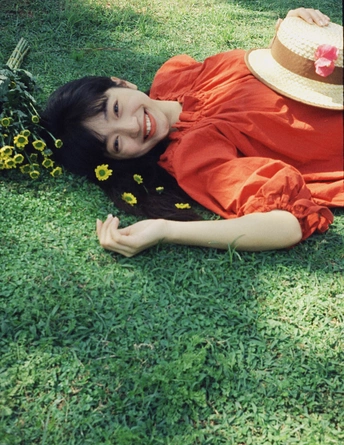 一个穿着裙子和帽子 躺在草地上 周围有黄色花朵的年轻女子