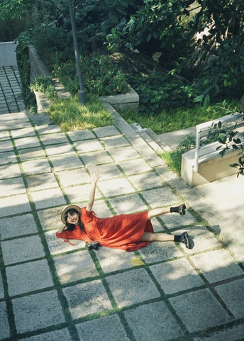 一位穿着红裙子的年轻女子躺在人行道上 双臂伸展。