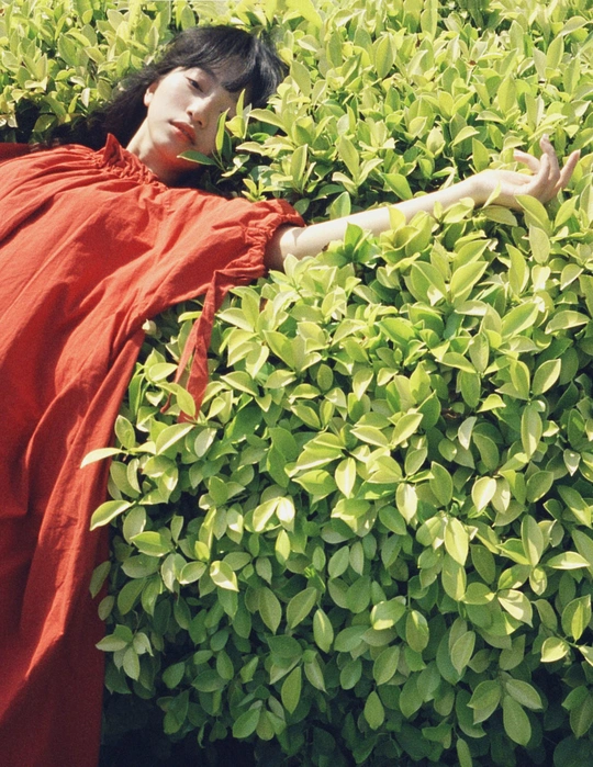 一位穿着红色连衣裙的女人在绿色灌木丛前摆姿势