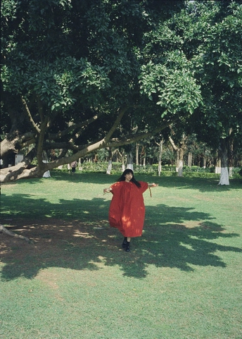 一位穿着红色连衣裙和斗篷的女士站在公园里 周围有树木和草地。