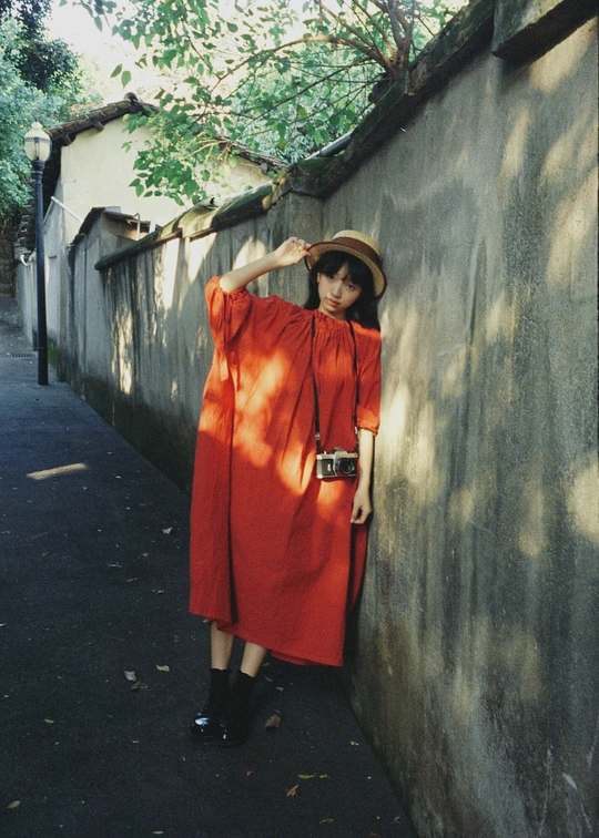 一位穿着红色连衣裙和帽子站在小巷里 倚靠在墙上的女人