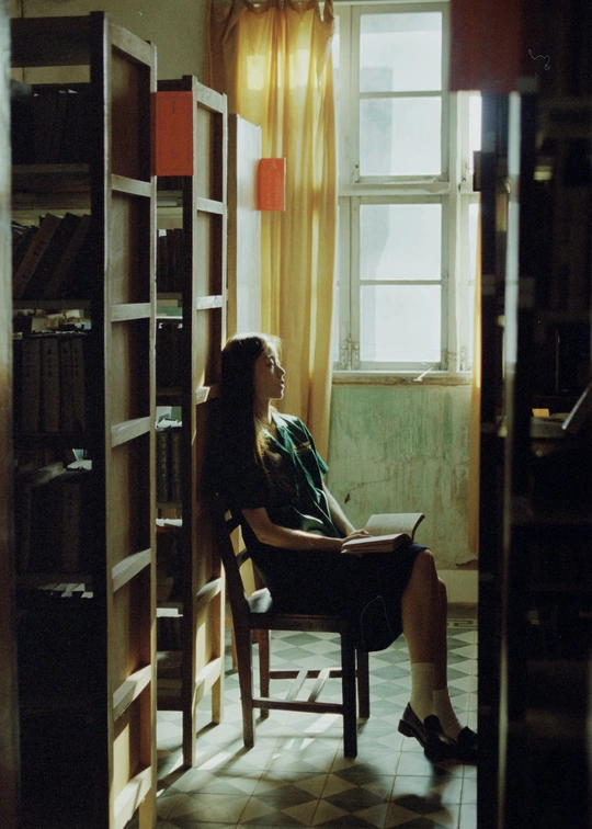 一个年轻女子坐在椅子上阅读一本书 房间里有书架和窗户。