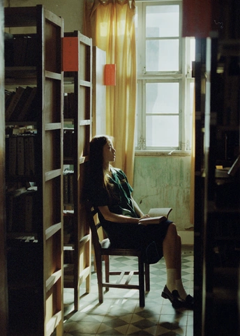 一个年轻女子坐在椅子上阅读一本书 房间里有书架和窗户。