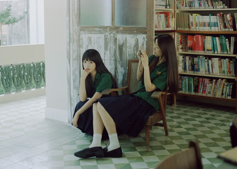 两个年轻女子坐在地板上有书的房间里 椅子上有书籍。