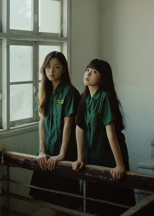 一些穿着绿色制服的年轻女孩站在一个有窗户的房间里 站在一根栏杆上。