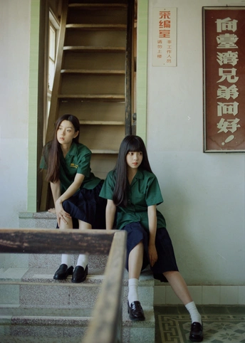 两个穿制服的女孩坐在一些台阶上 前面有一栋建筑。