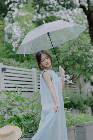 一位穿着蓝色连衣裙的年轻女子手持透明雨伞站在外面
