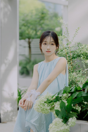 一位穿着蓝色连衣裙的年轻女子站在植物旁边