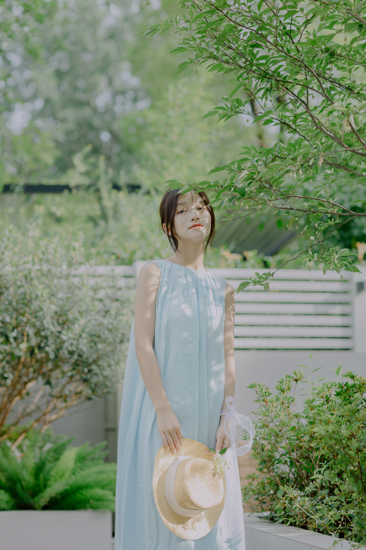 一位穿着蓝色连衣裙的年轻女子 戴着草编帽子 站在花园里。