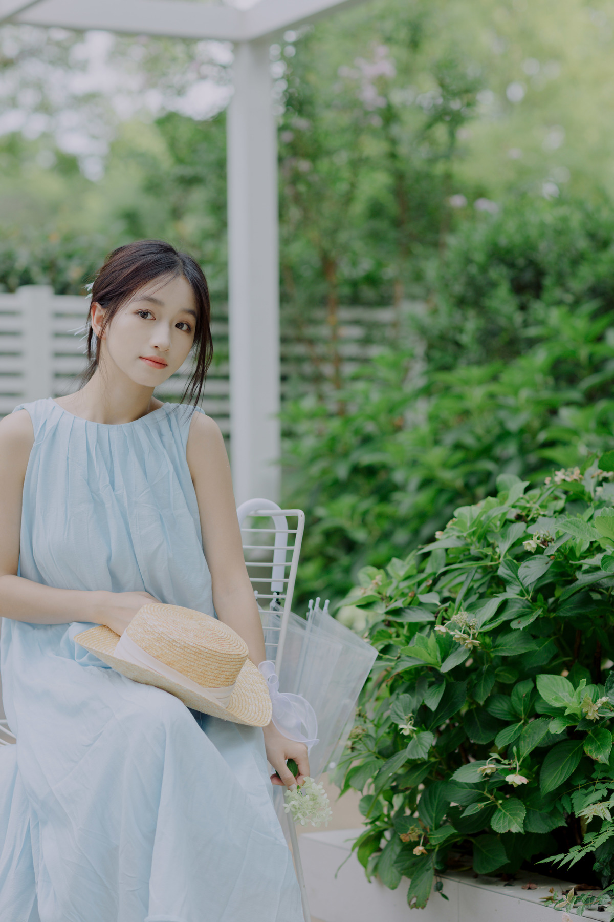 一位穿着蓝色连衣裙的美女坐在花园里的白色长凳上