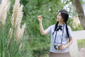 一位穿着制服的年轻女子手持相机站在高草前