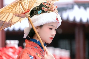一位穿着传统服装的年轻女子 戴着红白相间的帽子 手里拿着一把雨伞。