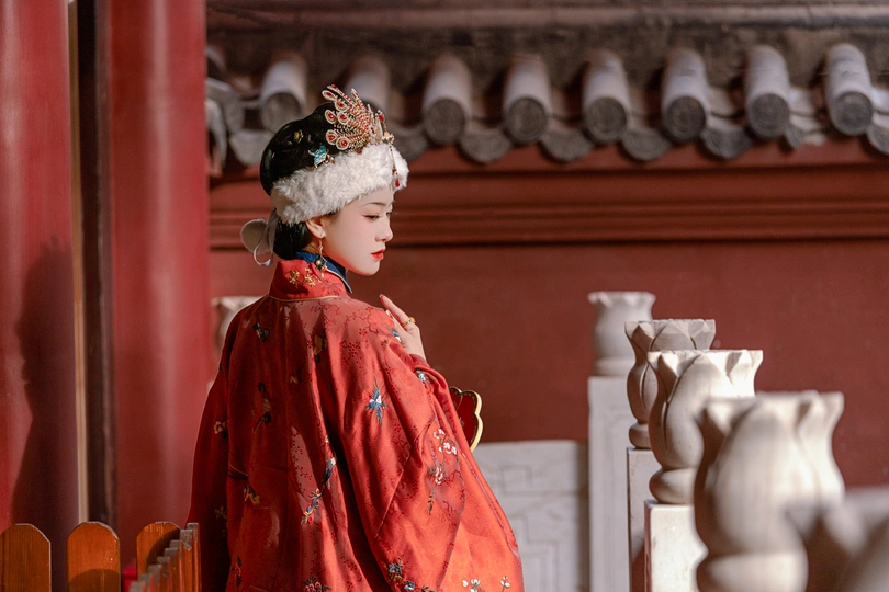 一位身着传统红色裙子的年轻女子站在一座寺庙的雕像前