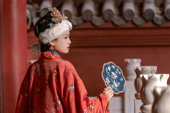 一个穿着传统红色和服和帽子拿着镜子的玩偶站在寺庙前的花瓶前。