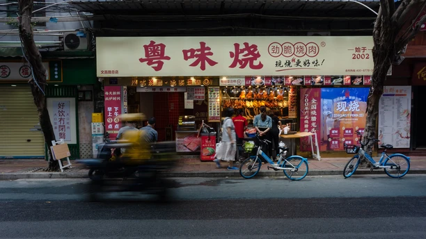 夜晚的城市街道 人们骑着自行车、滑板车和摩托车 停在商店前。