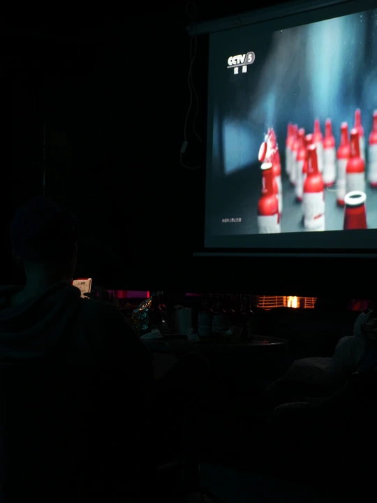 一个黑暗的房间 人们正在观看一个男子在大型屏幕上玩电子游戏。