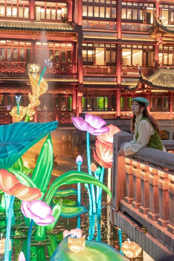 一位坐在建筑物前的遮阳伞下 水边有花的女人
