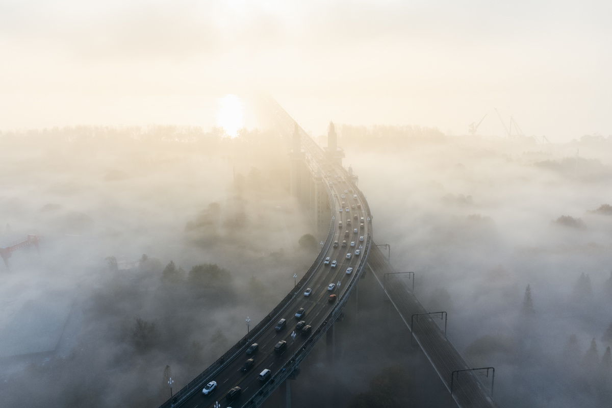 晨雾笼罩的城市 汽车在公路上行驶 阳光透过云层