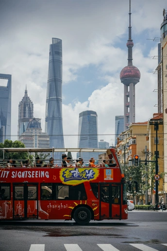 一辆红色的双层公交车在城市的街道上行驶 背景是高耸的建筑物。