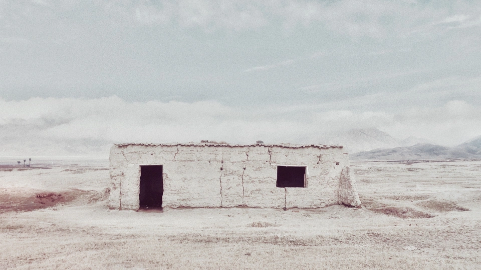 一个小屋坐落在一片荒凉的景观中 远处有山脉 前景中有一个被雪覆盖的田野。
