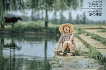 一个戴着帽子的小女孩坐在一个小池塘边上 一个小男孩在水中玩耍