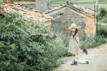 一个穿着连衣裙、戴着帽子的年轻女孩站在花园里的一块旧滑板上