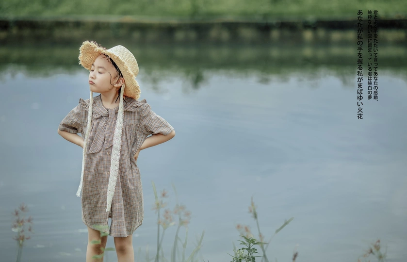 一个戴着草帽的小男孩站在池塘或河边看着水