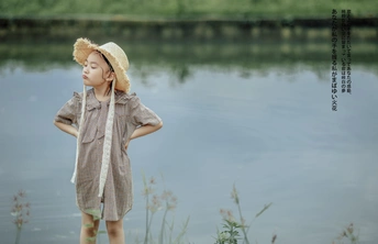 一个戴着草帽的小男孩站在池塘或河边看着水