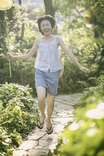 一位年轻女子拿着花和气球走在花园小径上