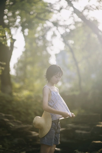一个戴草帽的年轻女子穿过森林 抱着一个小女孩。