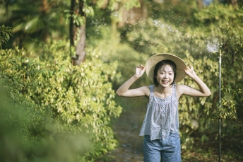 一位戴帽子站在花园里喷水自娱自乐的年轻女子