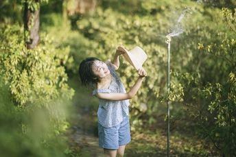 一个小女孩在给一棵年轻的树上喷水。