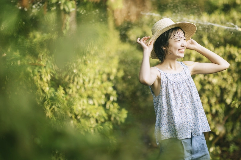 一位戴帽子站在花园里喷水管喷水的年轻女子