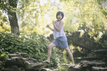 一位年轻女子站在一条溪流中的岩石上