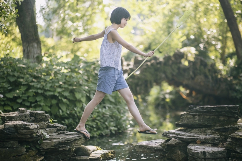 一个年轻男孩或女孩在河或小溪上跳过岩石 用绳子捕捉鱼。