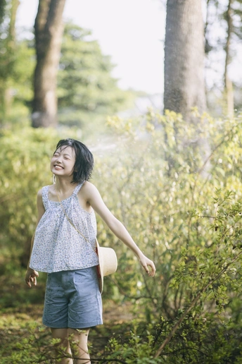 一位年轻女子戴着帽子 穿过一排树木时 举起双臂。