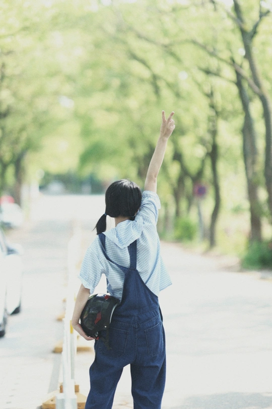 一个穿着工作服和背包的女人站在人行道上 她的手臂举过头顶 双手在空中。