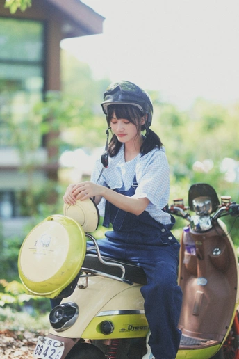 一个戴着头盔的小女孩坐在小型摩托车上 后面有一位女士骑着滑板车。