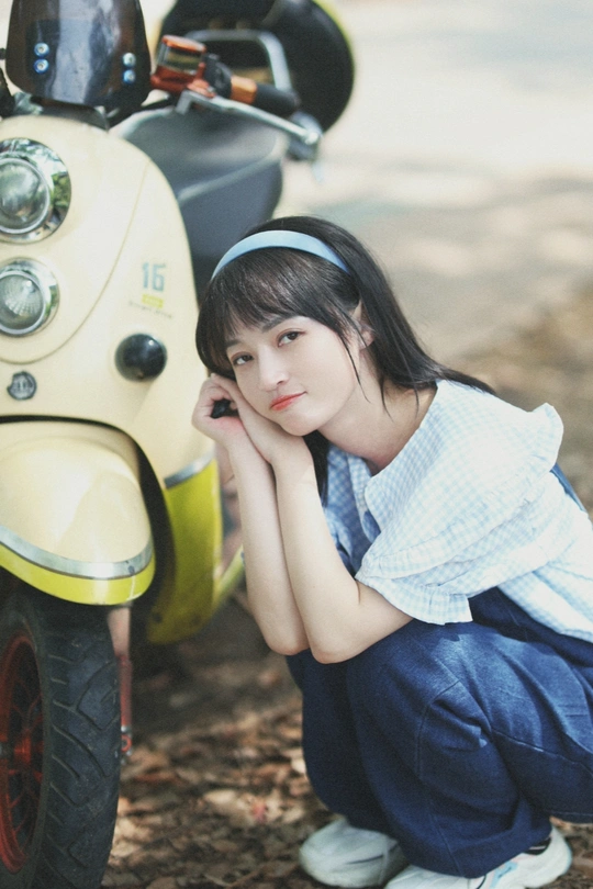 一位年轻女子靠在一辆黄色滑板上 坐在摩托车旁边。