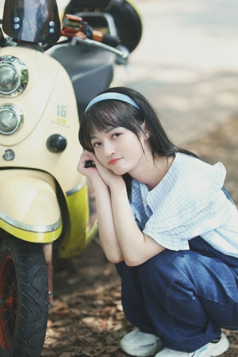 一位年轻女子靠在一辆黄色滑板上 坐在摩托车旁边。