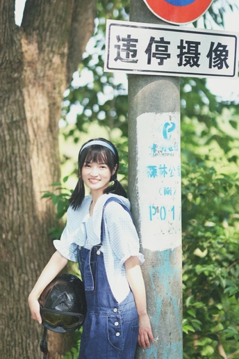 一位穿着工作服和头盔的年轻女子在树下举起街牌