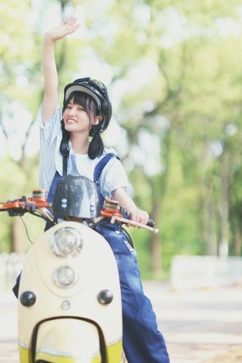 一个戴头盔的年轻女孩坐在摩托车上 双手举过头顶 一个小男孩在摩托车上骑着。