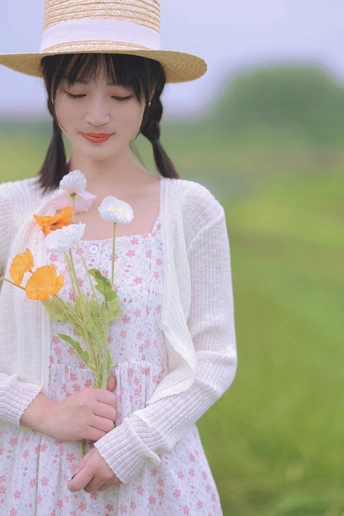 一位年轻女子戴着帽子 穿着一件漂亮的裙子 正在田野中拿着一束花。