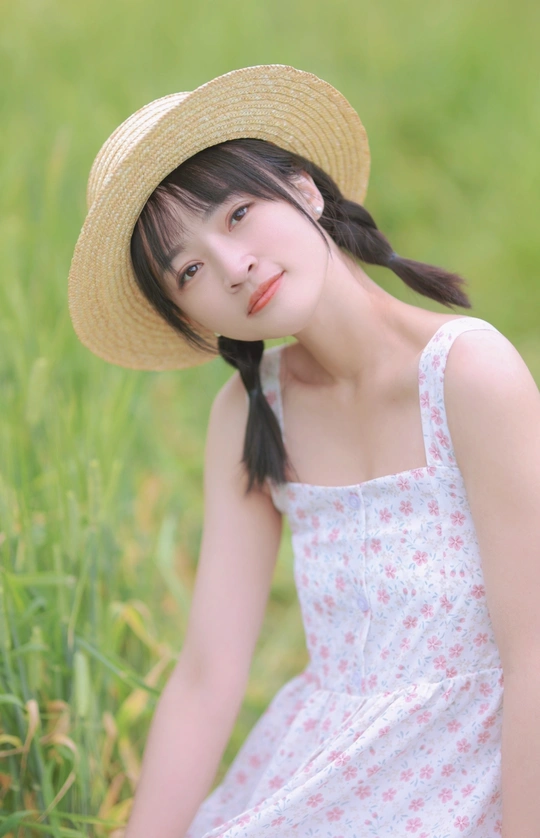 年轻美丽的女子戴着帽子穿着裙子坐在草地上的人物肖像