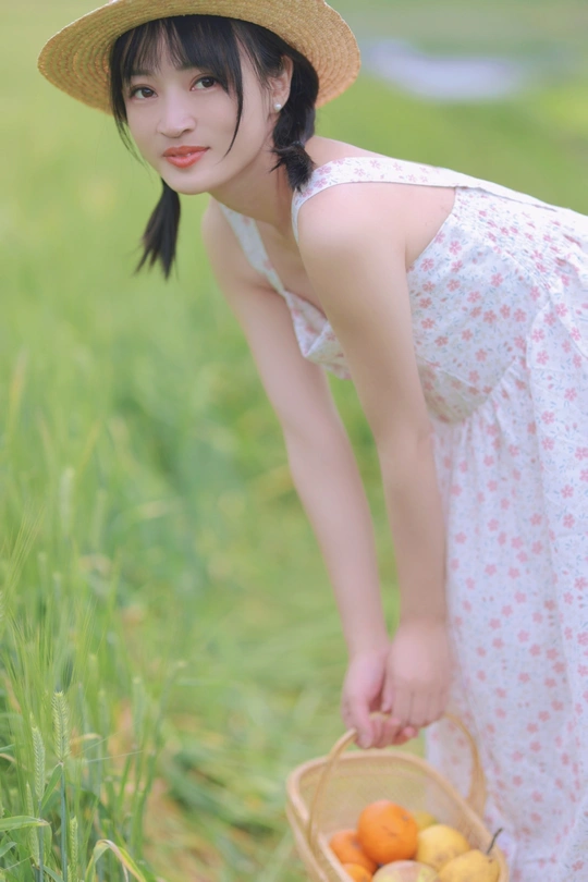 一位穿着连衣裙和草编帽子的年轻女子抱着一个装满水果的篮子