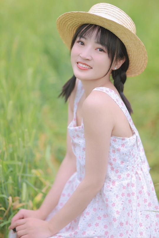 一位穿着白色连衣裙和草帽的年轻女子坐在草地上的一幅肖像画